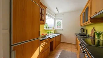 Funktionale Küche mit Holzschränken, dunkler Arbeitsplatte und Fenster mit Blick ins Freie.