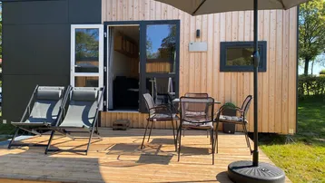 Moderne Tiny-House-Fassade mit Holzverkleidung und einer einladenden Holzterrasse mit Sitzgelegenheiten.