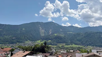 Panoramablick über die Dächer einer Stadt mit majestätischen Bergen im Hintergrund unter blauem Himmel.