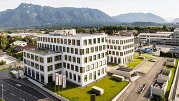 Luftaufnahme eines modernen Bürogebäudes mit weißer Fassade und Bergblick im Hintergrund.