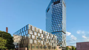 Moderne Hochhäuser mit Glasfassaden und einem niedrigeren Gebäudeteil unter blauem Himmel.