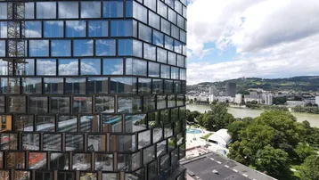 Modernes Hochhaus mit Glasfassade und Spiegelungen, bietet Blick auf Fluss und Stadt.