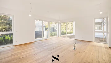 Helles und geräumiges Wohnzimmer mit großen Fenstern, Holzboden und Zugang zum Garten.