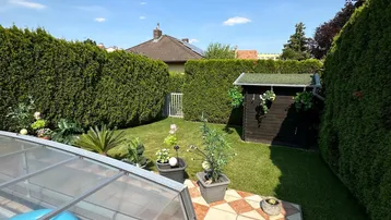 Gepflegter Gartenbereich mit Rasenfläche, hohen Hecken und einem überdachten Pool auf der Terrasse.