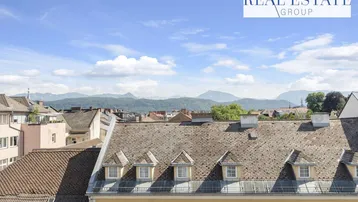 Panoramablick über die Dächer der Stadt mit majestätischen Bergen im Hintergrund.