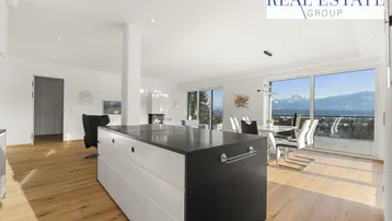 Heller offener Wohn-Essbereich mit moderner Küche, Holzboden und Panoramablick auf die Berge.
