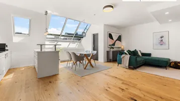 Heller offener Wohnbereich mit Holzboden, großen Dachfenstern, Essbereich und moderner Küche.