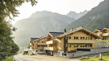 Moderne Holzfassaden der Gebäude in alpiner Landschaft mit Bergblick und Zufahrtsstraße.