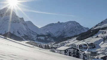 Winterliche Alpenlandschaft mit verschneiten Häusern und strahlendem Sonnenschein über den Bergen.