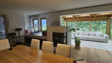 Offener Wohn-Essbereich mit Holztisch, Kamin und Zugang zu einem hellen Wintergarten.