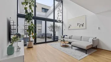 Helles Wohnzimmer mit hohen Decken, großen Fenstern und Zugang zu einem Innenhof.