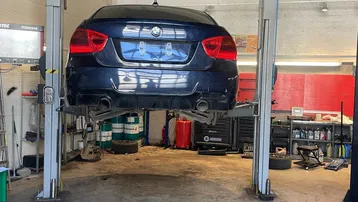 Geräumige Autowerkstatt mit einem Fahrzeug auf einer hydraulischen Hebebühne und einem Betonboden.