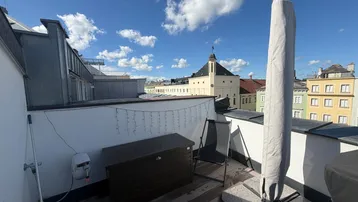 Dachterrasse mit Holzboden, Stadtblick und Platz für Outdoor-Möbel unter blauem Himmel.