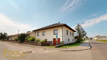 Einfamilienhaus an einer Straßenecke mit umliegender Grünfläche und klarem Himmel.