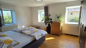 Helles Schlafzimmer mit Holzboden, großen Fenstern und Blick ins Grüne.