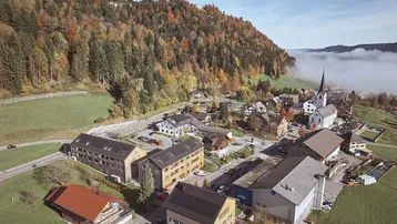 Luftaufnahme eines malerischen Dorfes in einer Herbstlandschaft mit bunten Bäumen und Nebel in der Ferne.