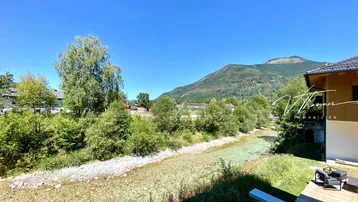 Weitblick auf den klaren Fluss, die grüne Landschaft und die umliegenden Berge.