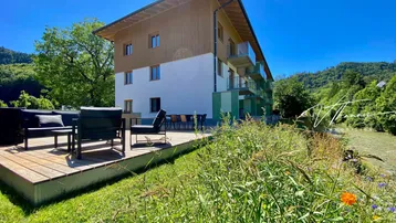 Geräumige Holzterrasse mit modernen Gartenmöbeln und Blick auf die umliegende Natur und Berge.