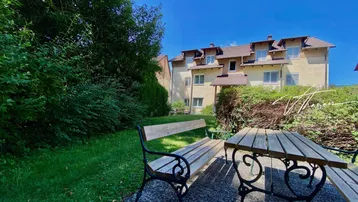 Gartenbereich mit Sitzgelegenheiten und Blick auf das Mehrfamilienhaus unter blauem Himmel.
