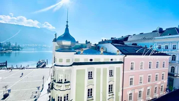 Panoramablick über die Stadt und den See mit historischen Gebäuden unter strahlendem Sonnenschein.