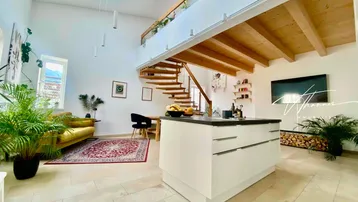 Heller, offener Wohnbereich mit hoher Decke, Galerie, Holztreppe und moderner Kücheninsel.