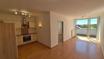 Heller offener Wohnbereich mit integrierter Küche, Laminatboden und Zugang zu einem sonnigen Balkon.