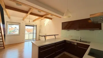 Heller offener Wohnbereich mit integrierter Küche, Holzbalken und Zugang zu einem Balkon.
