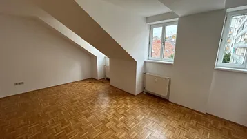 Helles Zimmer mit Parkettboden, weißen Wänden und Dachschrägen, ideal als Wohn- oder Schlafzimmer.