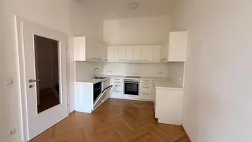 Moderne Einbauküche mit weißen Schränken, integrierten Geräten und elegantem Fischgrätparkettboden.