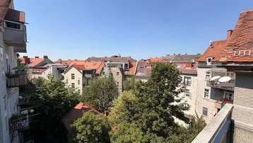 Ausblick vom Balkon über die Dächer der Stadt mit viel Grün und Bäumen.