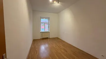 Geräumiger, heller Raum mit Holzparkettboden und einem Fenster, das den Blick nach draußen freigibt.