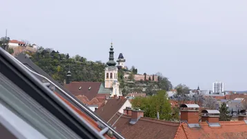 Panoramablick über die Dächer der Stadt mit historischem Uhrturm und grüner Hügellandschaft.