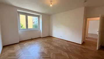 Helles Zimmer mit Fischgrätparkettboden und Blick ins Grüne, bereit zur individuellen Gestaltung.