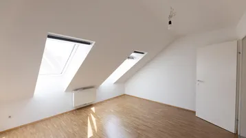 Helles Dachzimmer mit Holzboden und zwei Dachfenstern, ideal als Schlaf- oder Arbeitszimmer.