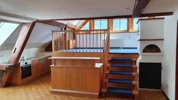 Geräumiger offener Wohnbereich mit integrierter Küche, Holztreppe und traditionellem Kaminofen.