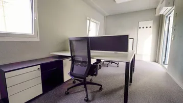 Modernes Büro mit Schreibtischen, Bürostühlen und Fenstern, die viel Tageslicht hereinlassen und eine angenehme Arbeitsatmosphäre schaffen.