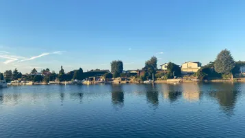 Ruhige Seeansicht mit Häusern am Ufer unter einem weiten, klaren blauen Himmel.