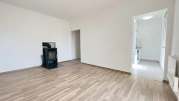 Helles Wohnzimmer mit Holzofen und Parkettboden, mit Zugang zu einem weiteren Raum.