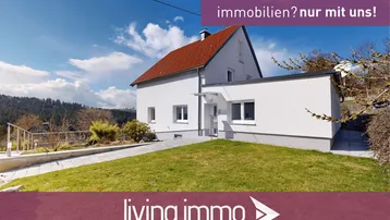 Weißes Einfamilienhaus mit rotem Ziegeldach und gepflegtem Vorgarten in ländlicher Umgebung.