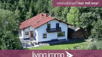 Luftaufnahme eines Einfamilienhauses mit rotem Dach, umgeben von dichtem Wald und viel Grün.