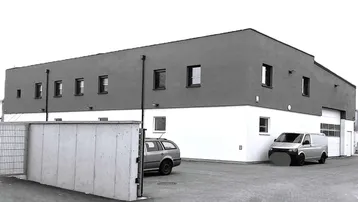 Modernes Geschäftsgebäude mit zweifarbiger Fassade und Parkplätzen davor, unter einem bewölkten Himmel.