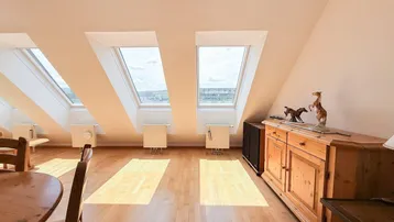 Helles Dachgeschosszimmer mit Holzboden, Dachfenstern und Blick auf die Umgebung.