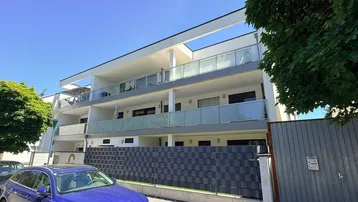Modernes Mehrfamilienhaus mit mehreren Balkonen und klaren Linien unter blauem Himmel.