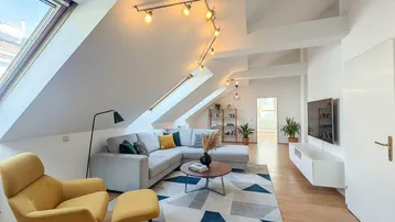 Helles und modern eingerichtetes Wohnzimmer im Dachgeschoss mit schrägen Decken, großem Dachfenster und Holzboden.