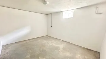Leerer Kellerraum mit Betonboden, weiß gestrichenen Wänden und einem kleinen Fenster.