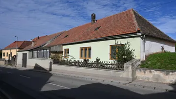 Älteres Wohnhaus mit hellgrüner Fassade, rotem Ziegeldach und Holzzaun an der Straße.