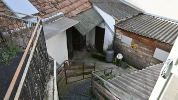 Blick von oben auf den Hinterhof mit Außentreppe, Schuppen und verschiedenen Dächern, die eine Renovierung benötigen.