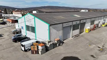 Luftaufnahme eines Industriegebäudes mit Parkplätzen und Baumaterialien im Freien unter blauem Himmel.