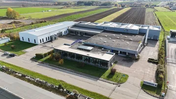 Luftaufnahme eines großen Gewerbekomplexes mit mehreren Hallen und umliegenden Feldern unter klarem Himmel.