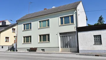 Vorderansicht eines älteren Wohnhauses mit hellgrüner Fassade und mehreren Fenstern.